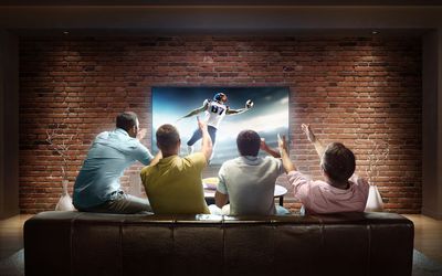 Quatro homens assistindo a um jogo de futebol