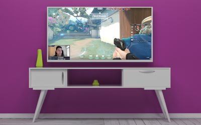 Um stream do Twitch passando em uma TV em uma sala roxa.