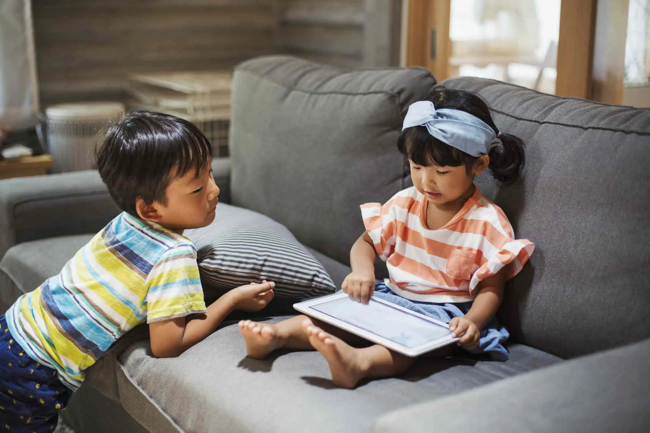 Duas crianças em um sofá usando um computador tablet. 