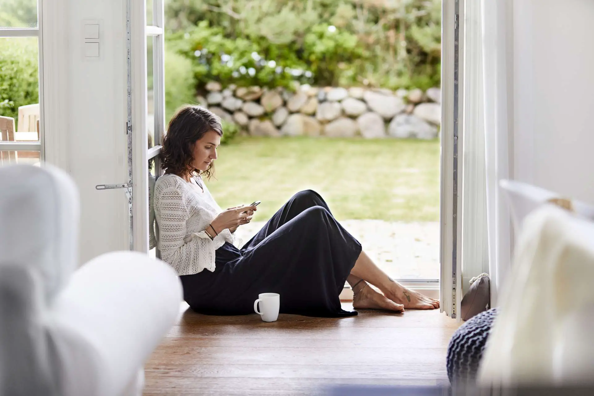 Uma mulher sentada perto de uma porta aberta, verificando o celular.