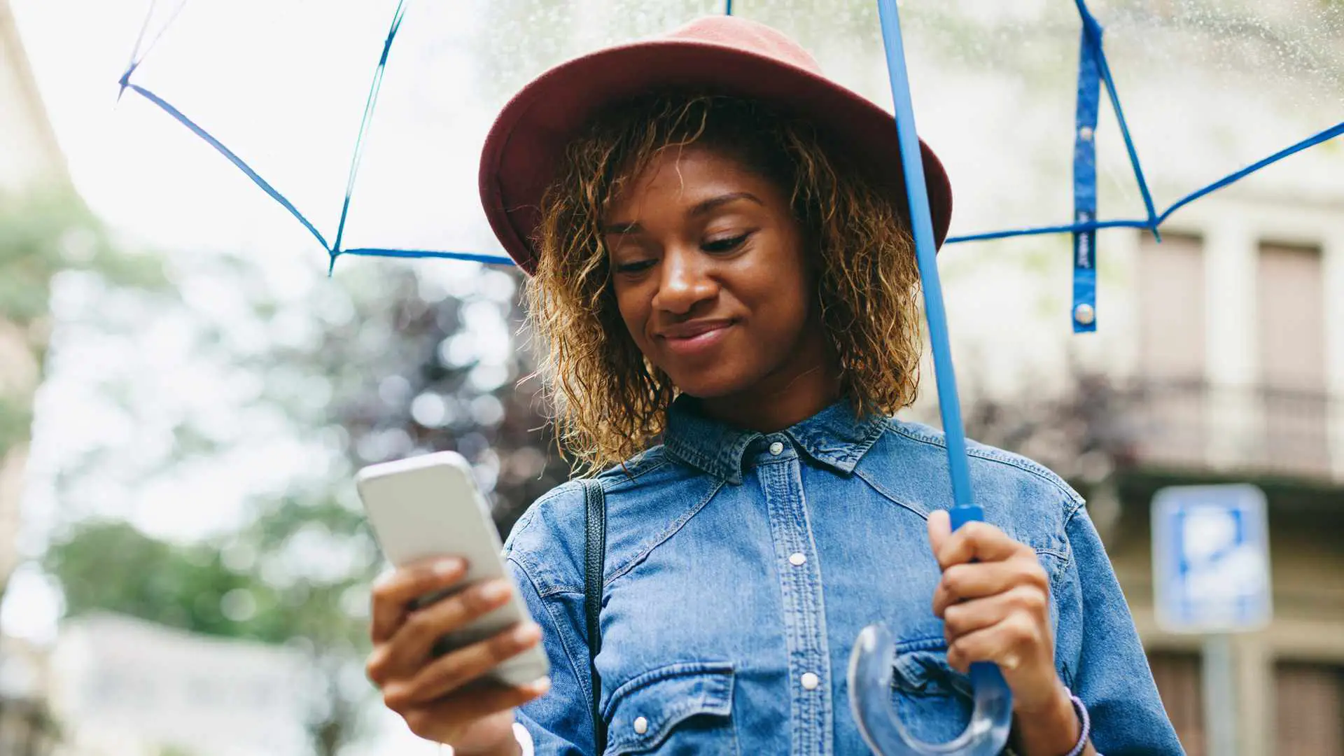 Mulher parada na chuva com um guarda-chuva, verificando o aplicativo de clima do iPhone
