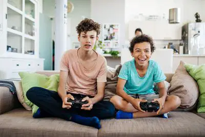 Dois meninos sentados em um sofá sorrindo com controladores de jogos nas mãos