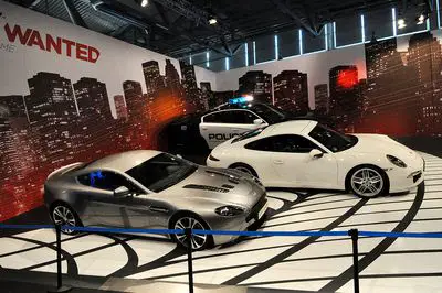 Carros da vida real em frente ao pôster de parede Need for Speed ​​Most Wanted