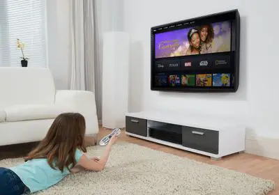 Uma jovem deitada em um tapete enquanto assiste a um filme infantil no serviço de streaming do Disney Plus em uma TV,
