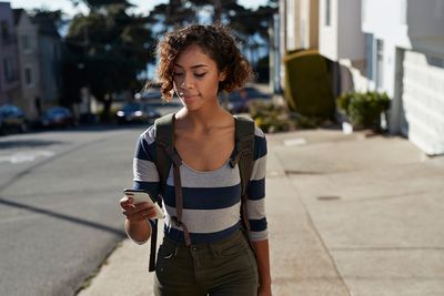 Mulher caminhando em uma estrada íngreme e olhando para o smartphone
