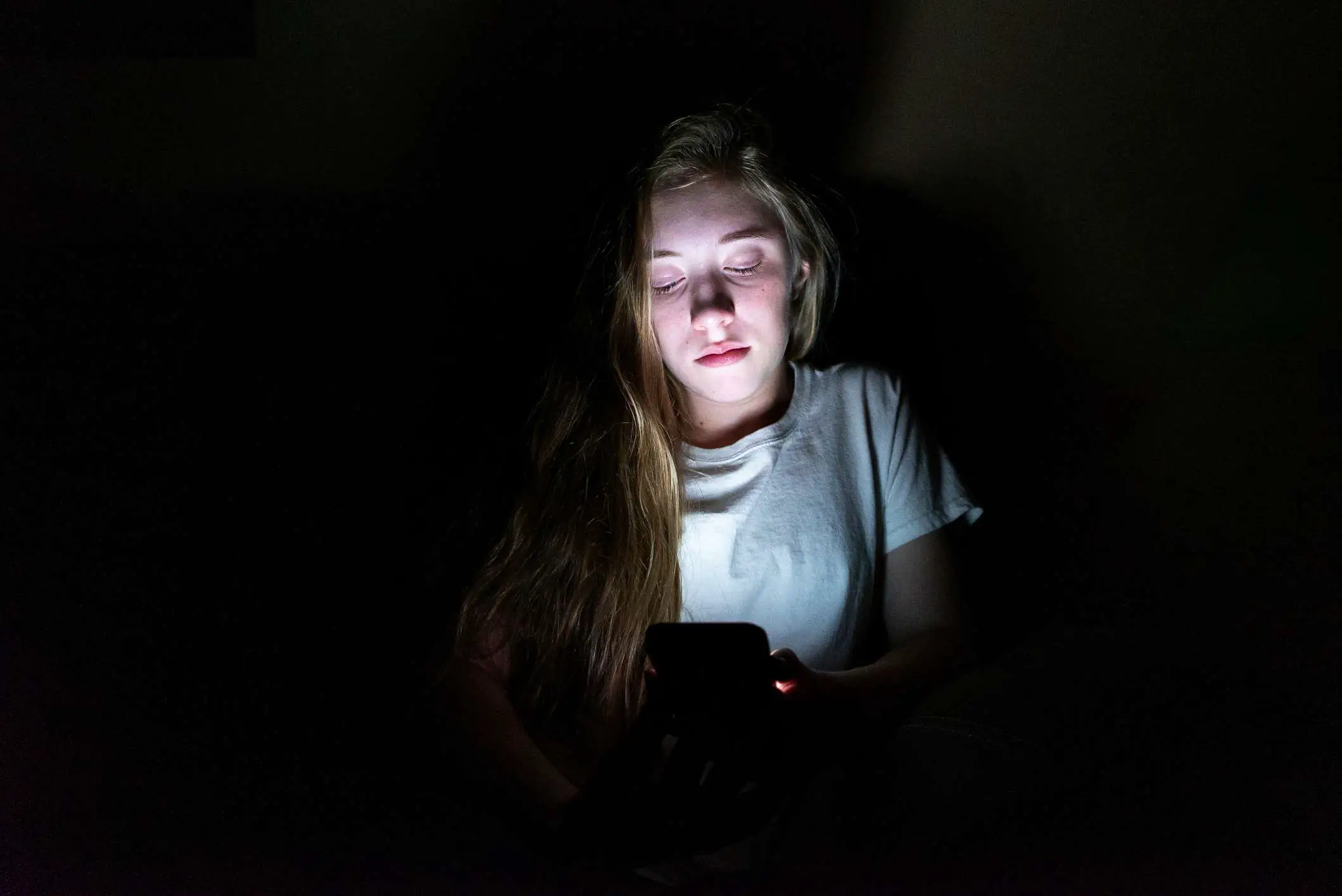 Um adolescente usando um smartphone no escuro. 