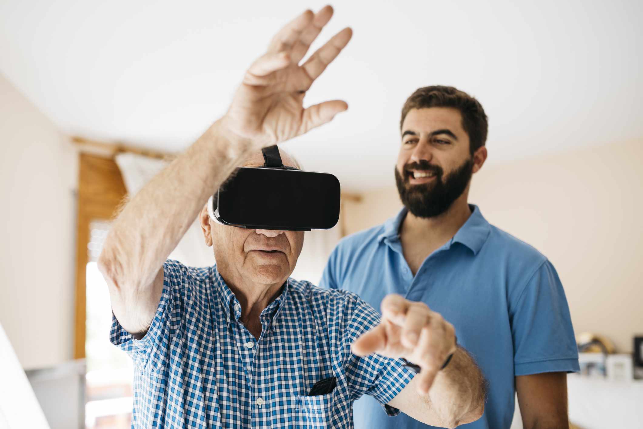 Homem sênior usando óculos de realidade virtual em casa enquanto seu neto adulto o observa