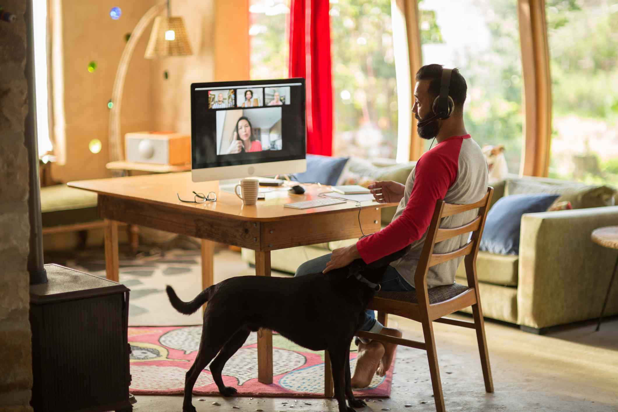 Homem trabalhando em casa em seu computador e acariciando seu cachorro durante o confinamento