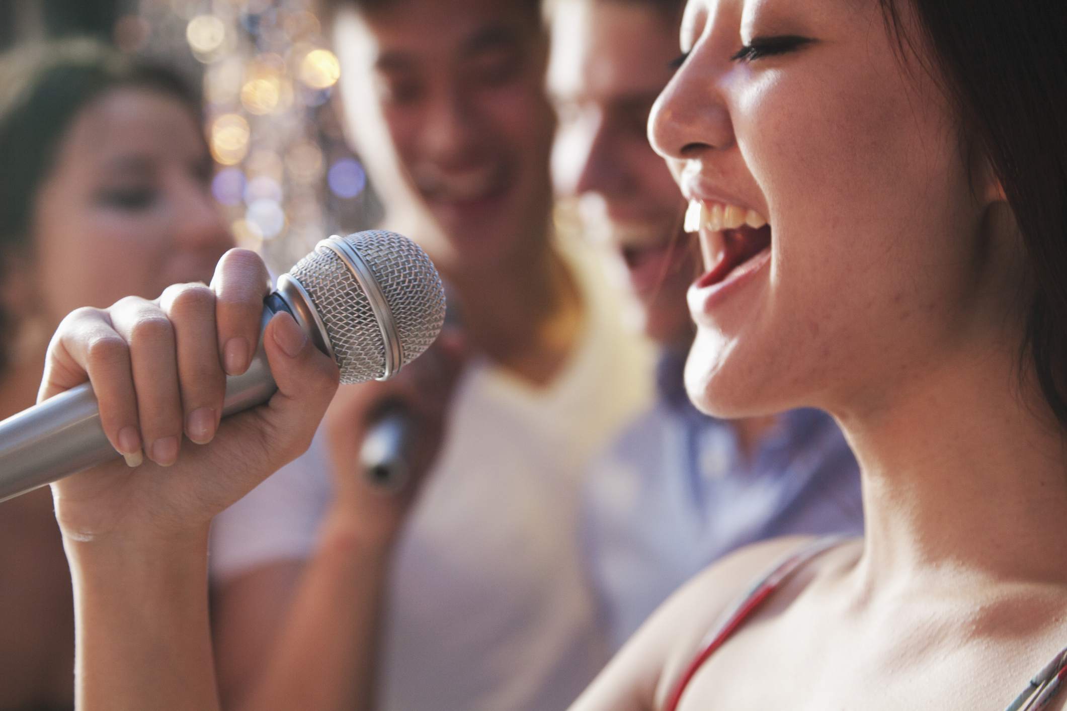 Close de uma mulher cantando em um microfone com amigos ao fundo