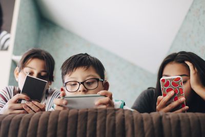 Uma foto de três crianças em uma cama, todas usando smartphones
