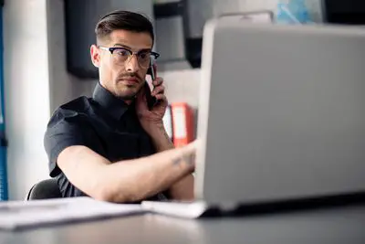 Homem de óculos no telefone usando um laptop