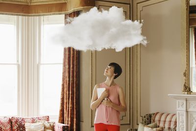 Mulher na sala de estar olhando para uma nuvem acima da cabeça