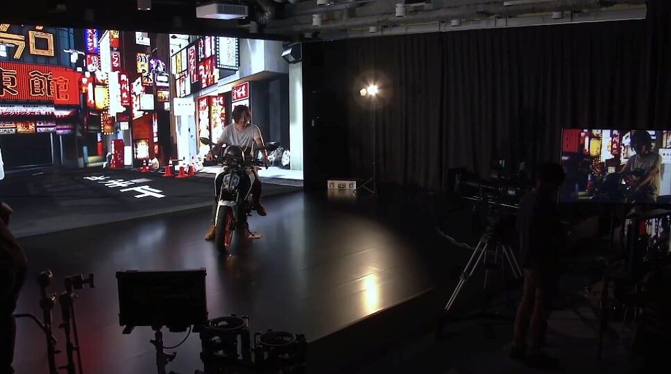 Ator em uma motocicleta em frente a uma tela virtual