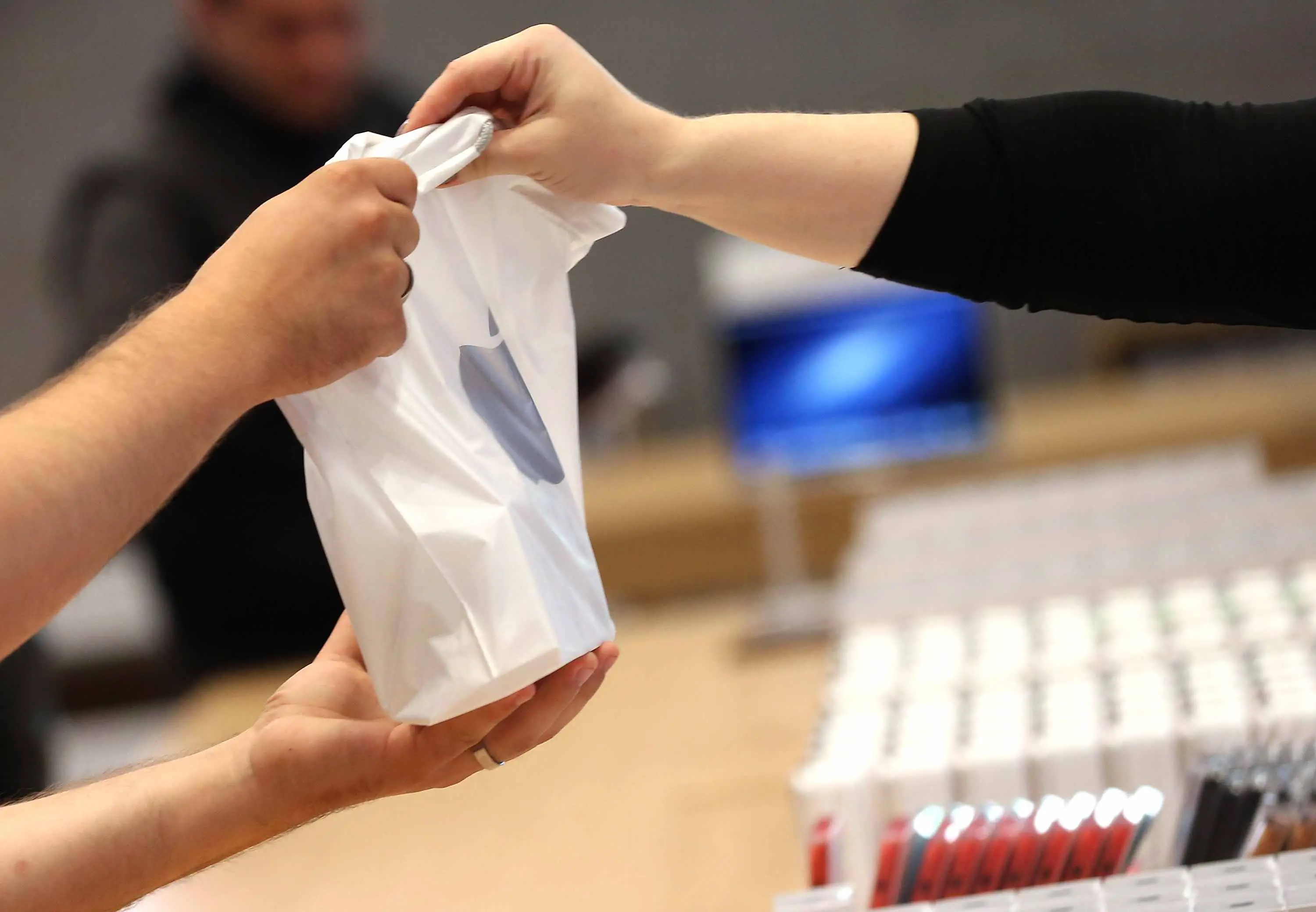 Feche as mãos e uma sacola do funcionário e do cliente durante uma compra em uma Apple Store.