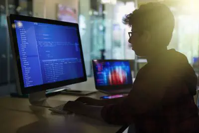 Estudante de menino programando computador em sala de aula escura