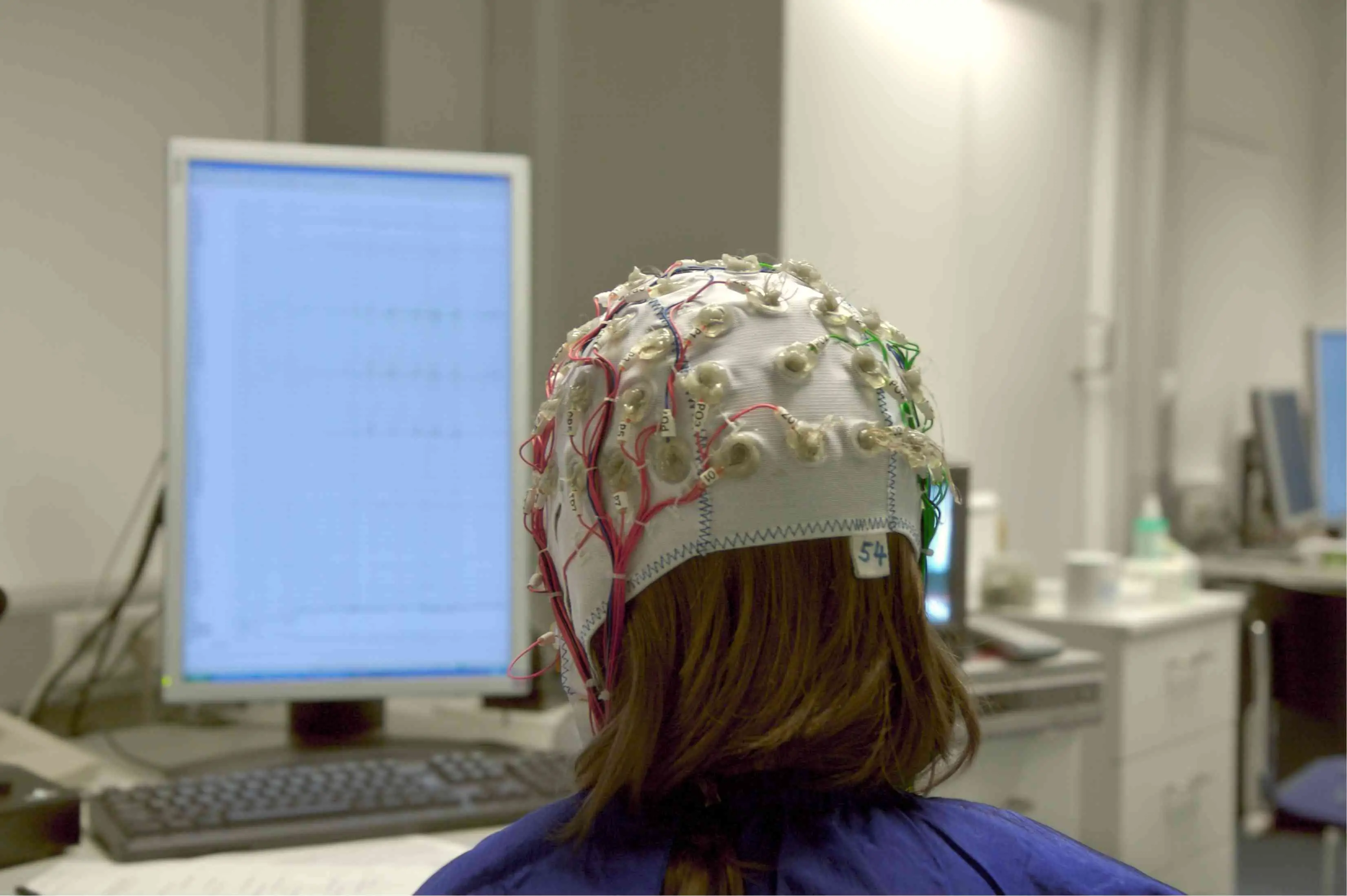 A visão por trás de alguém conectado a uma máquina de EEG sentado em frente a uma tela de computador. 