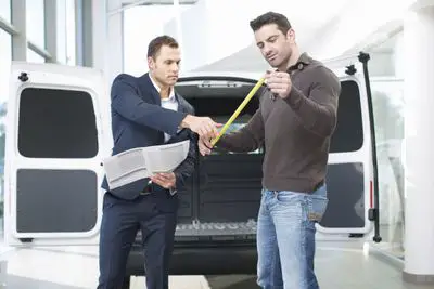 Dois homens na frente de uma van com uma fita métrica