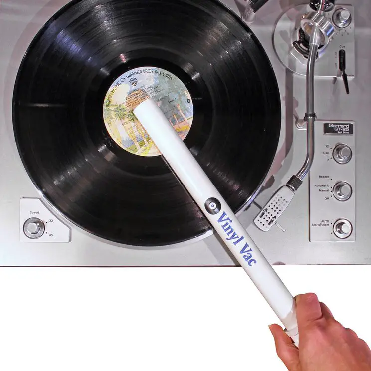 Uma mão segurando um Vinyl Vac para limpar um disco que está em cima de uma plataforma giratória