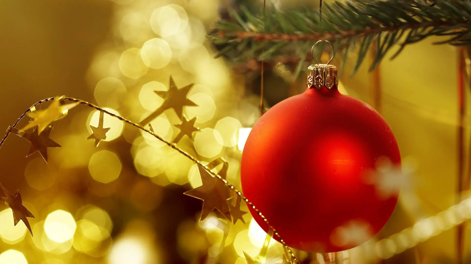 Papel de parede de Natal grátis com uma lâmpada vermelha em uma árvore de Natal com fundo dourado brilhante