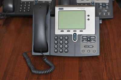 Foto conservada em estoque de um telefone de mesa IP da Cisco Systems sentado em frente a dois outros telefones em uma mesa.
