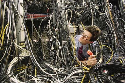 Trabalhador de computador enterrado em cabos de rede, segurando o plugue
