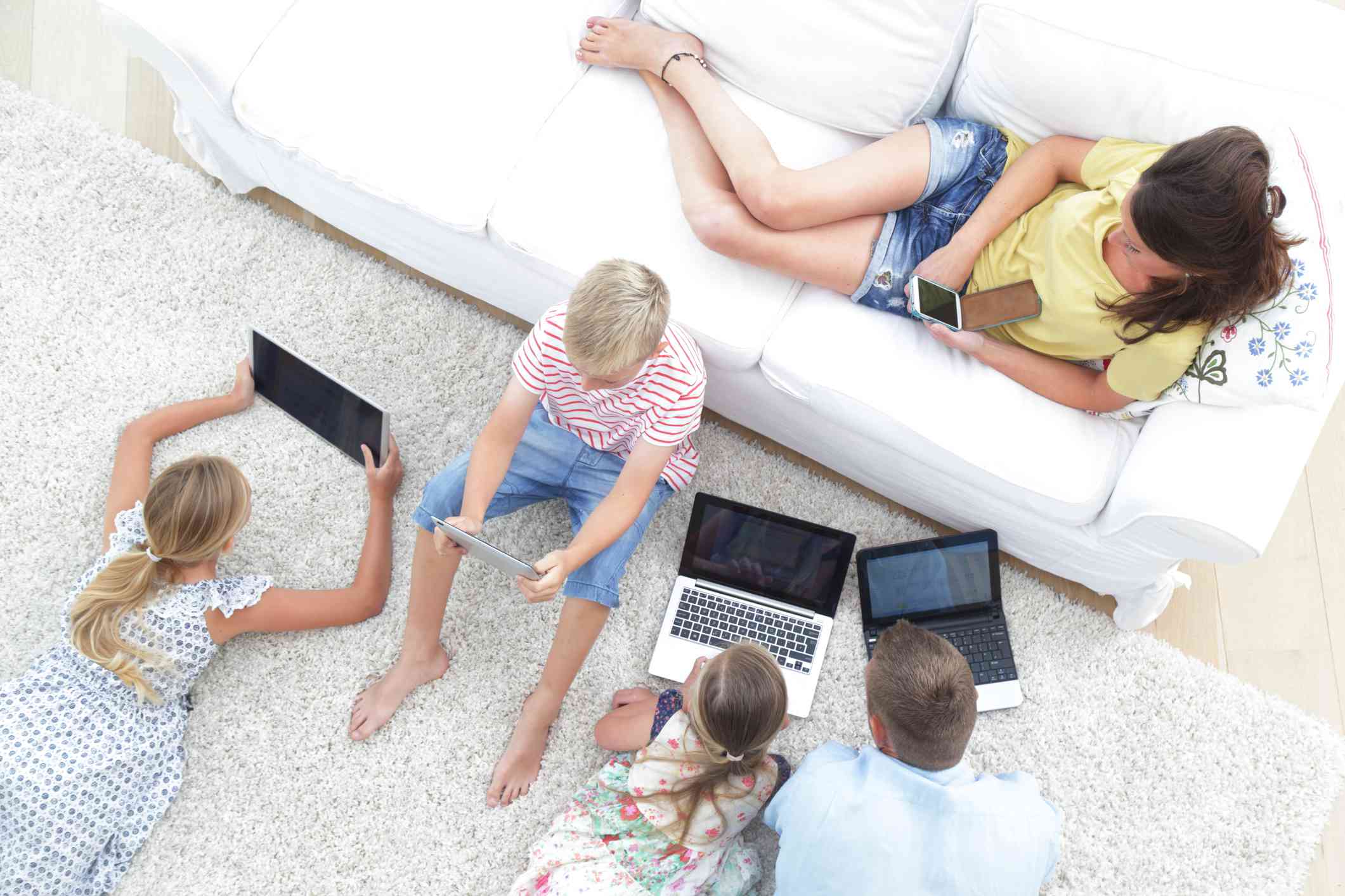 Uma família de cinco pessoas, todos usando dispositivos de tecnologia na sala de estar. 