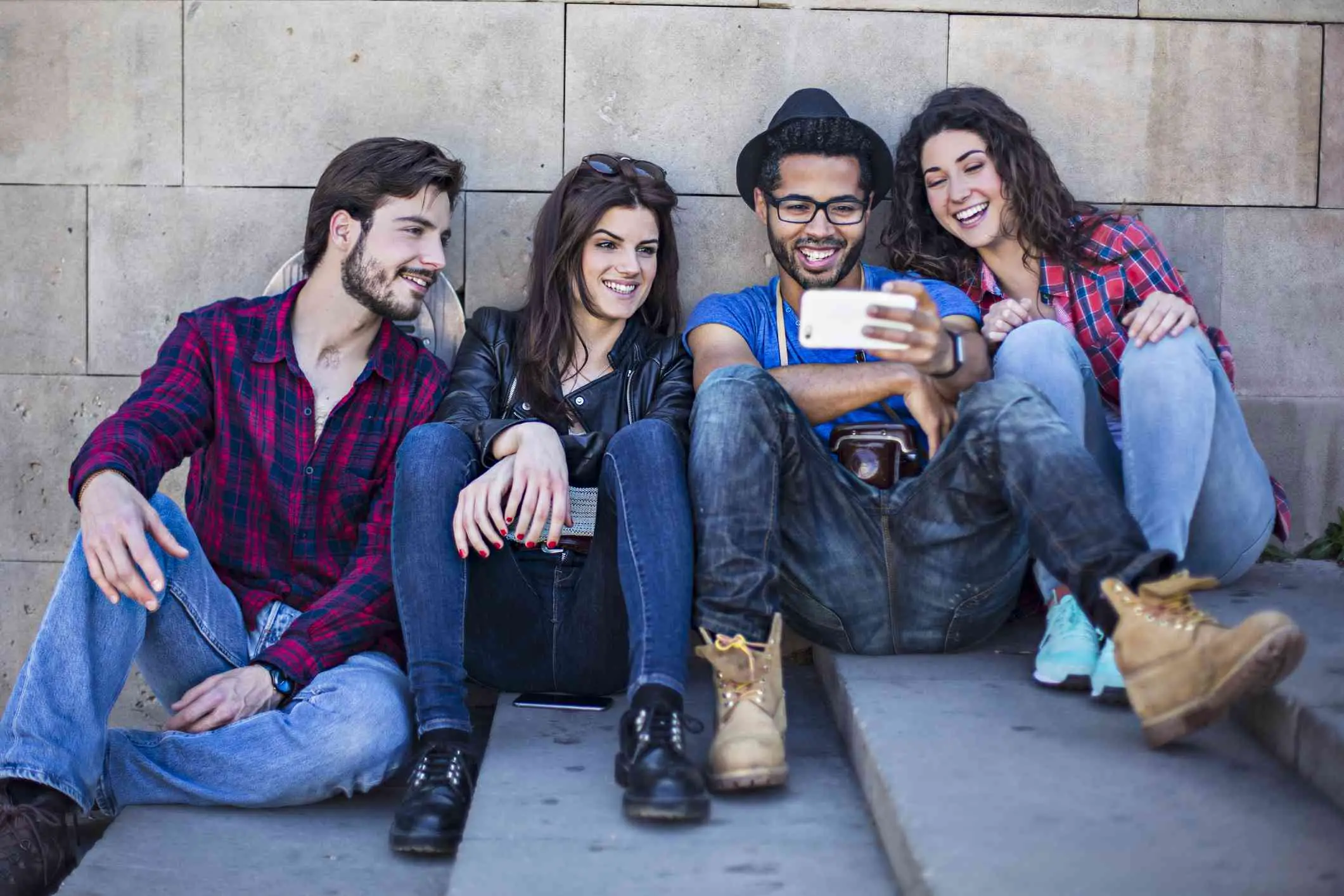 Quatro amigos assistindo a um filme em um smartphone, sentados ao ar livre em escadas de concreto.