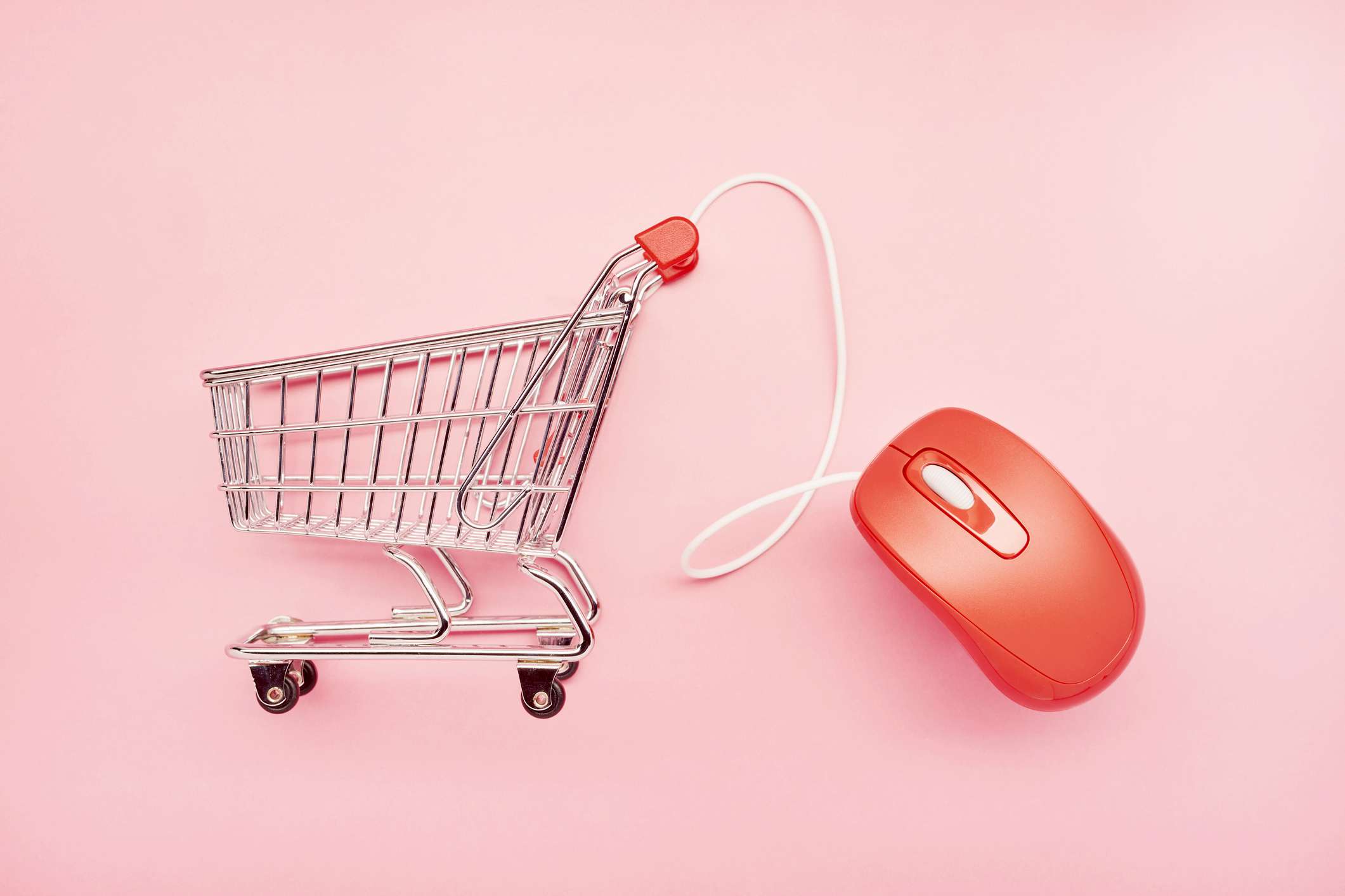 Natureza morta de um pequeno carrinho de compras e do mouse vermelho do computador em um fundo rosa, compras online
