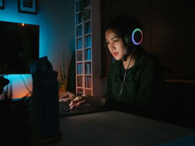 Uma mulher sentada no escuro usando fones de ouvido com um laptop na frente dela