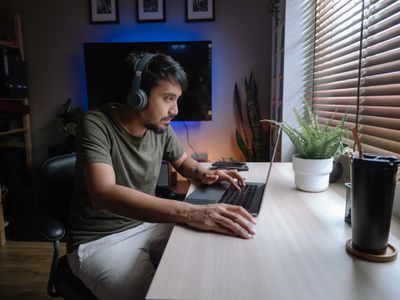Um homem usando fones de ouvido, sentado em uma mesa com um laptop na frente dele