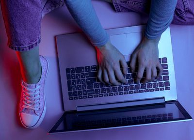 Uma mulher vestindo jeans roxos, camiseta e sapatos digitando em seu laptop.