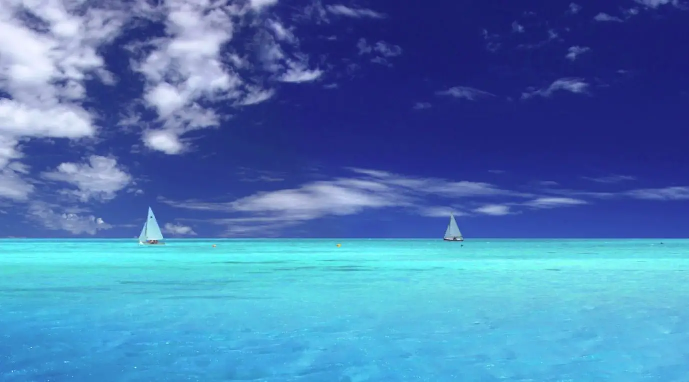 Papel de parede gratuito do oceano com veleiros brancos distantes em um oceano azul claro sob um céu azul com nuvens dispersas
