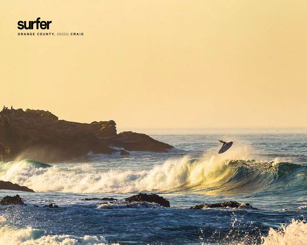 Papel de parede gratuito do oceano com um surfista no meio do salto acima de uma onda perto de rochas e penhascos