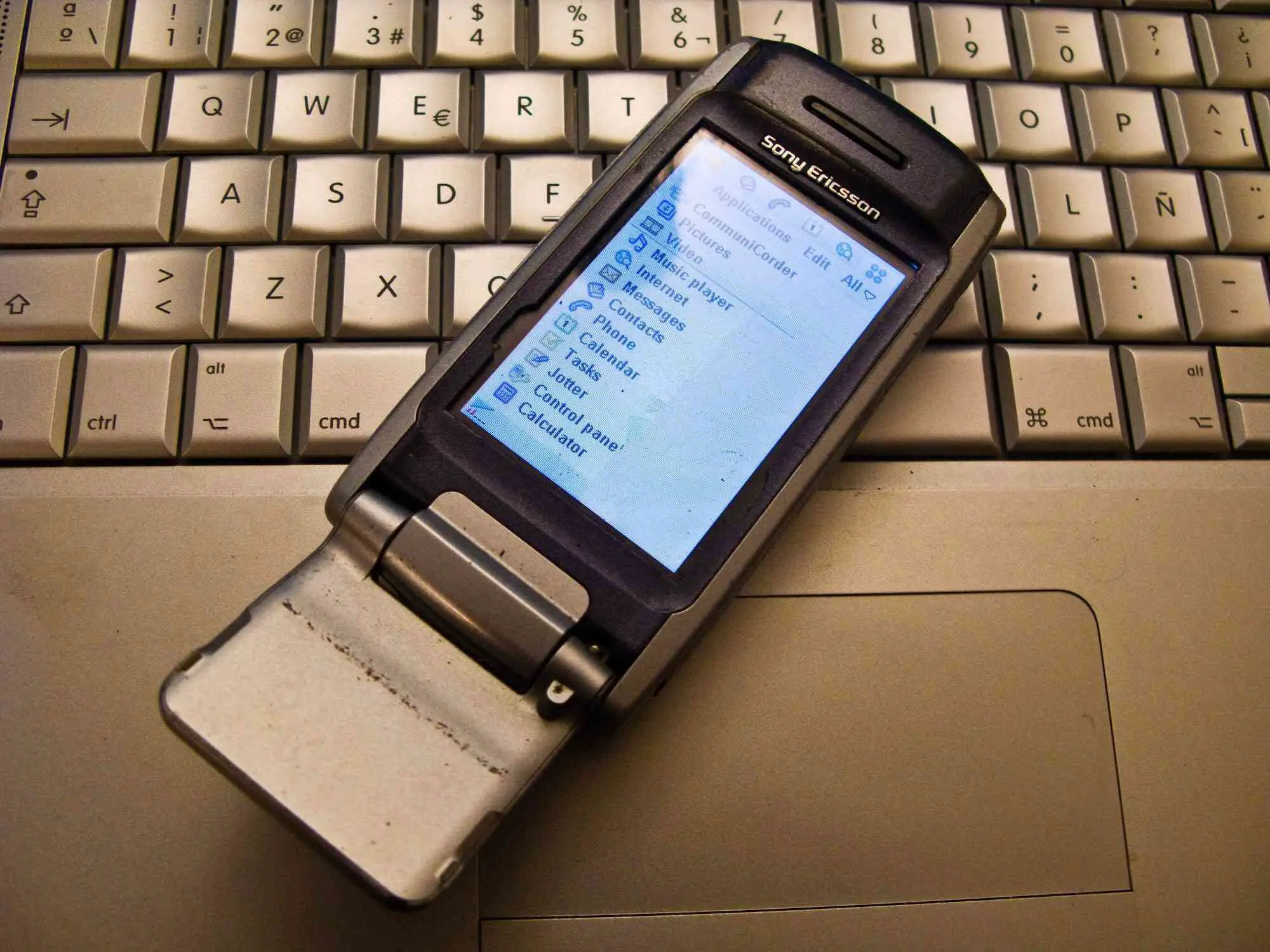 Foto de um velho celular Sony Ericsson apoiado em um laptop