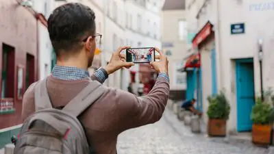 Um homem usando uma mochila e tirando uma foto com seu smartphone durante uma viagem internacional.