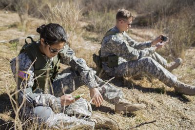 Dois militares da ativa usando seus telefones em campo.