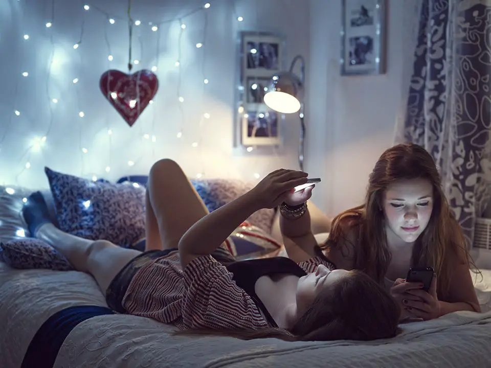 Meninas sentadas na cama olhando para telefones