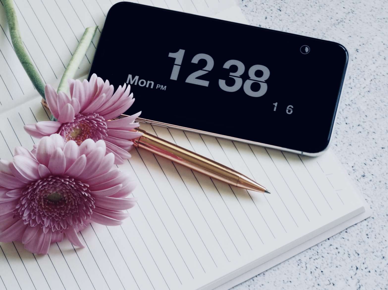 iPhone mostrando as horas enquanto descansa em um notebook com uma caneta