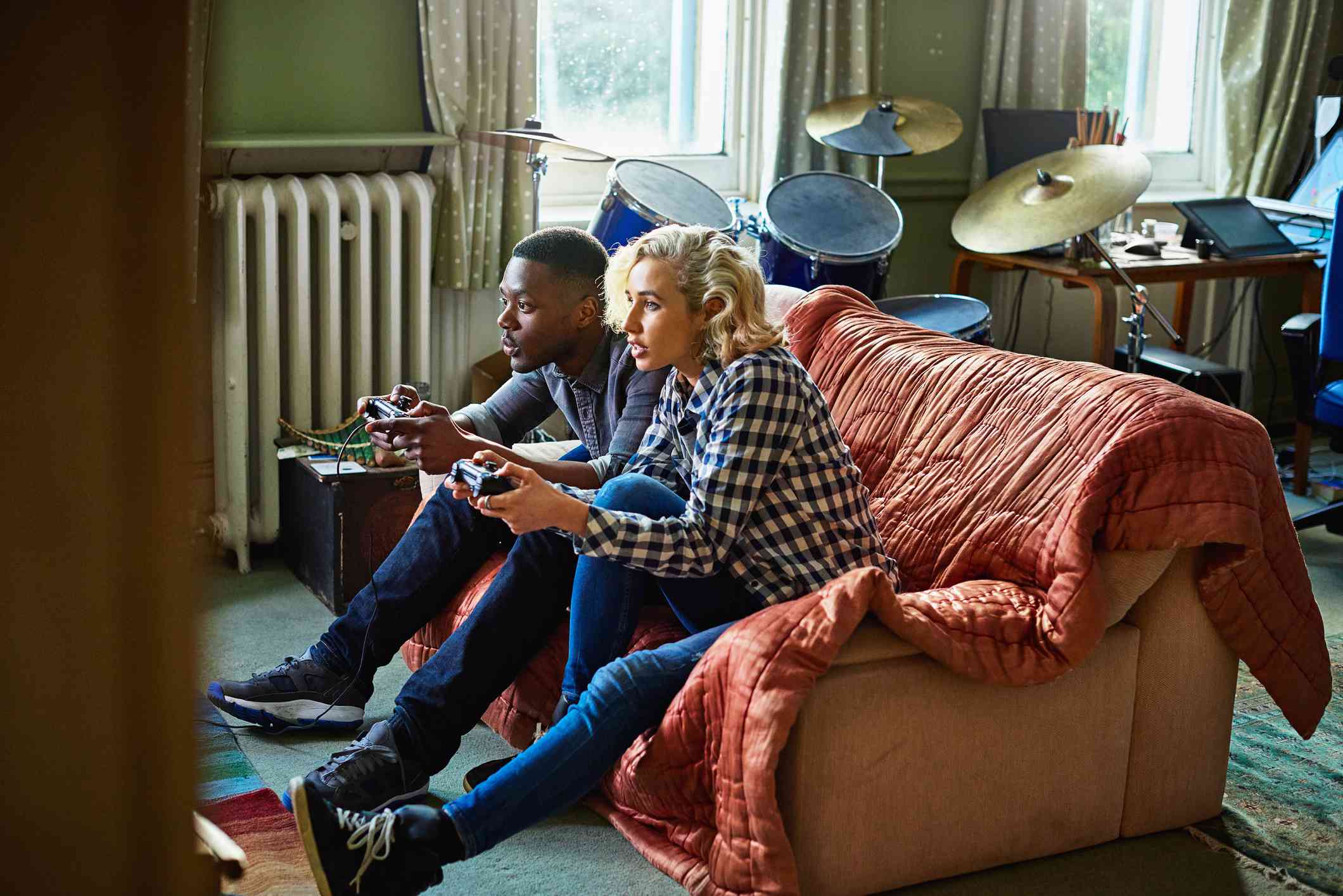 Dois jovens adultos jogando videogame, sentados em um sofá em um pequeno apartamento.