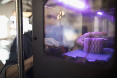 Uma mão alcançando uma impressora 3D