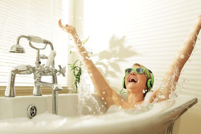 Uma mulher com óculos de sol verdes e fones de ouvido, chapinhando na banheira