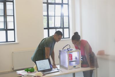 Dois designers olhando para uma impressora 3D