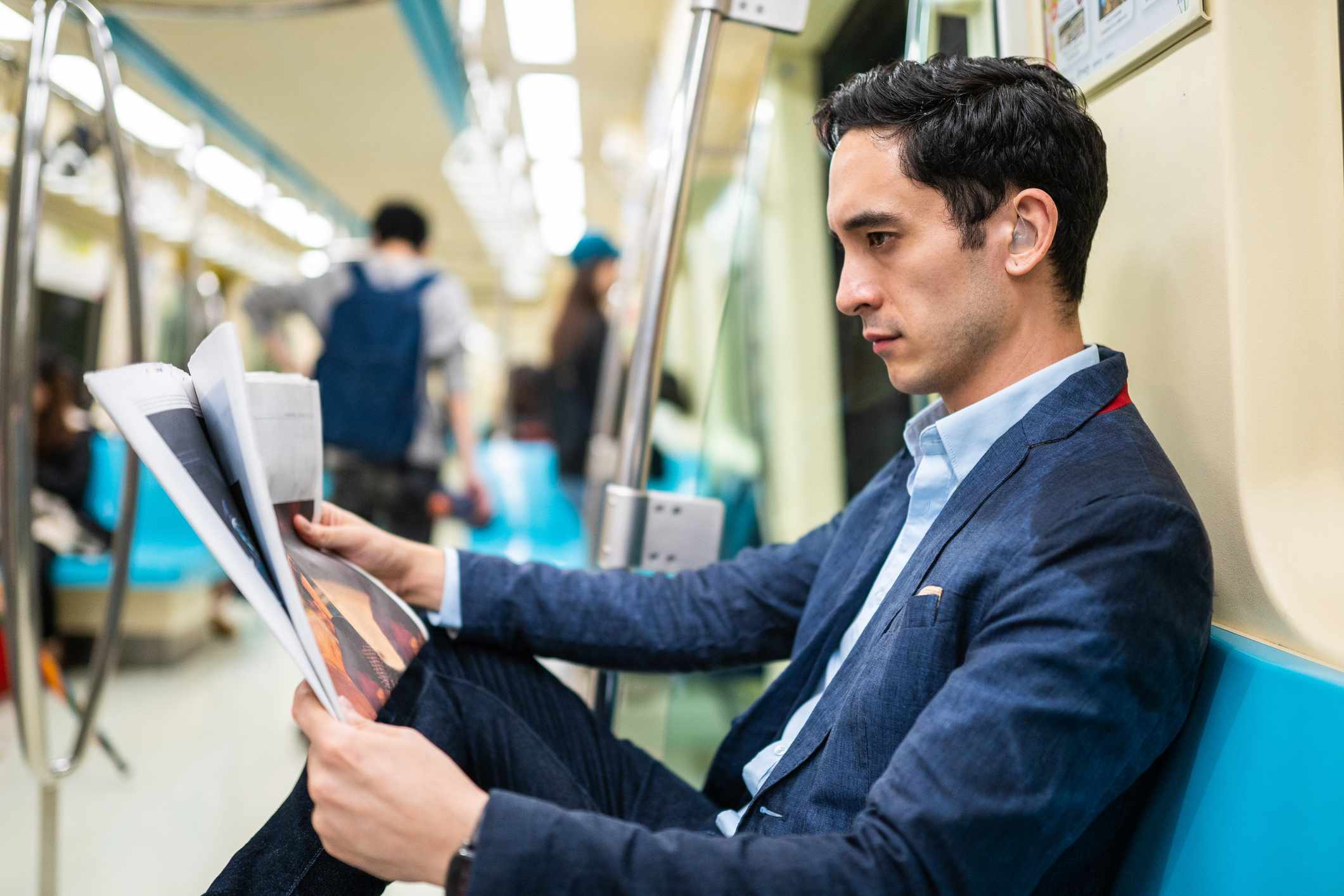 Alguém usando um dispositivo para melhorar a audição enquanto lê um jornal no trem. 
