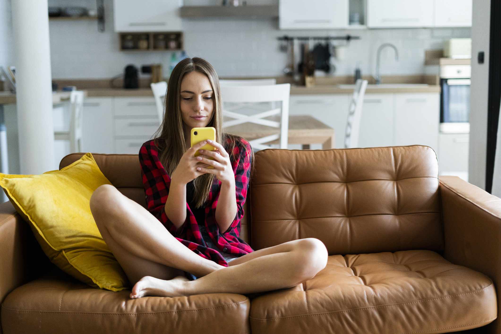 Um jovem usando um smartphone enquanto está sentado em um sofá em casa.