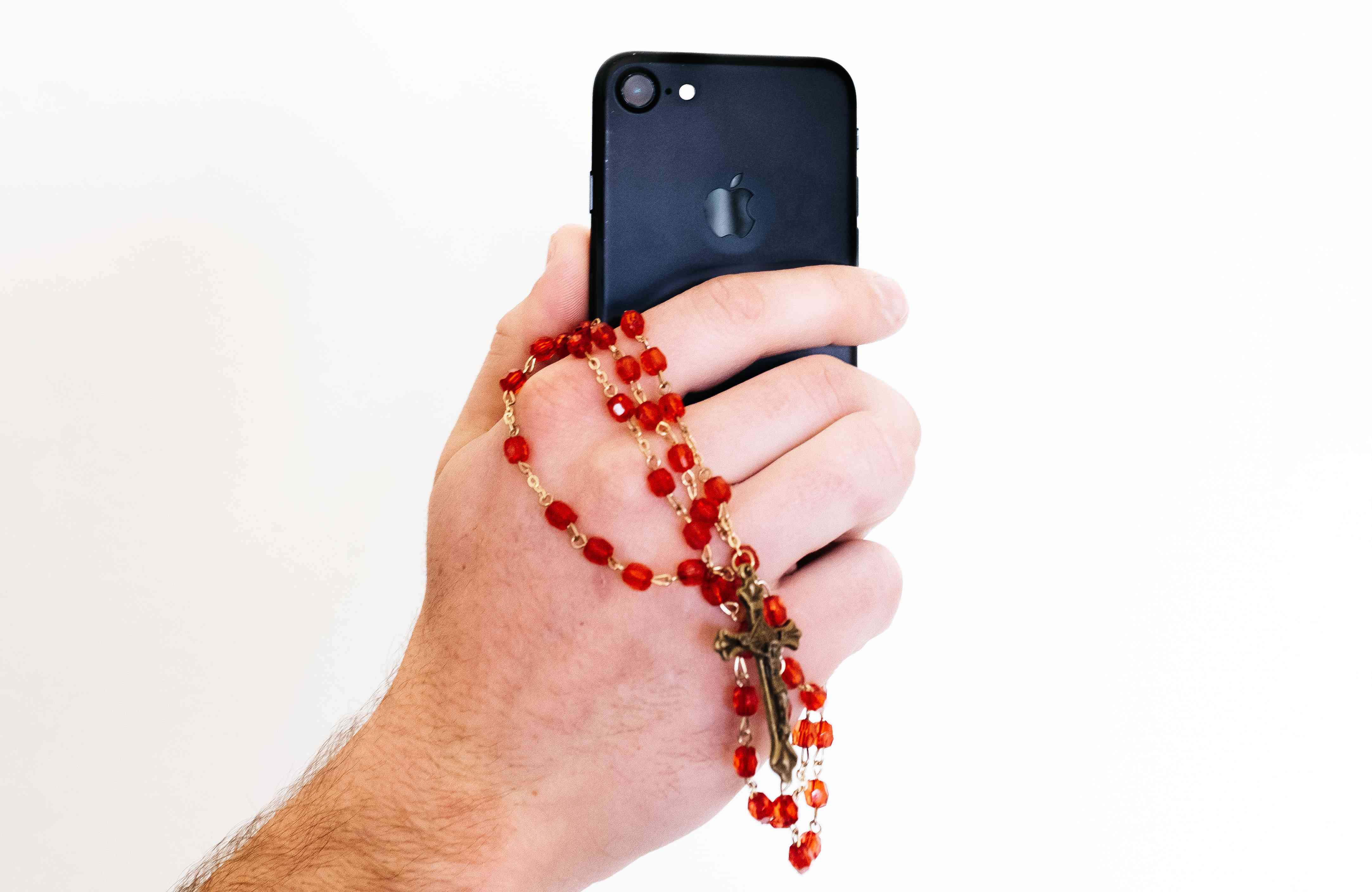 Um close de uma mão segurando um smartphone e um rosário.