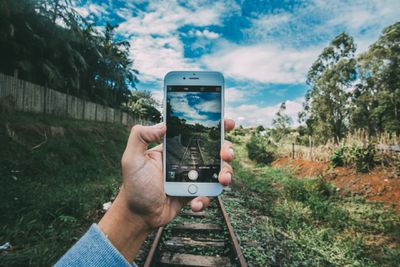 Mão segurando o iPhone na frente dos trilhos da ferrovia