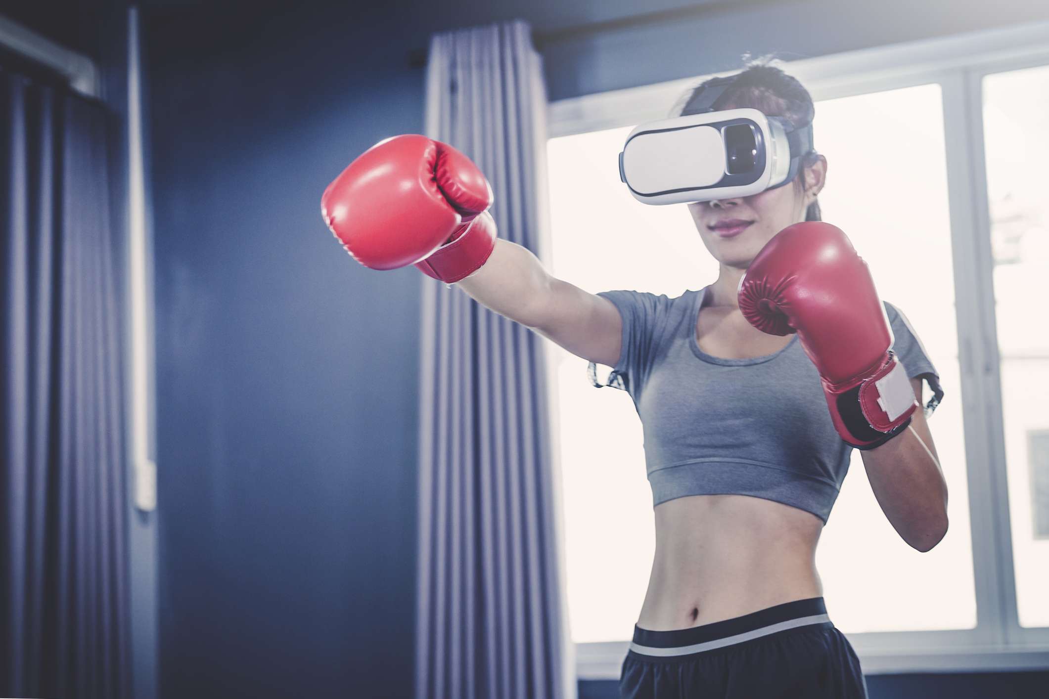 Uma mulher usando um fone de ouvido de realidade virtual e luvas de boxe. 