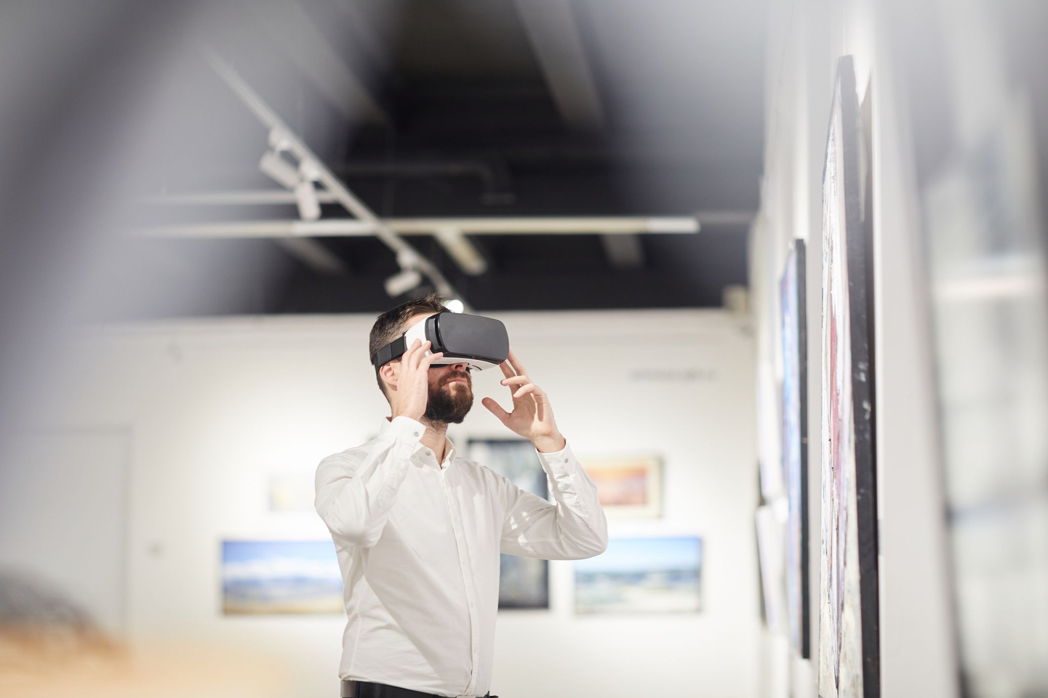 Vista lateral de alguém usando o equipamento de realidade virtual enquanto desfruta de uma experiência imersiva durante uma exposição em uma galeria de arte. 