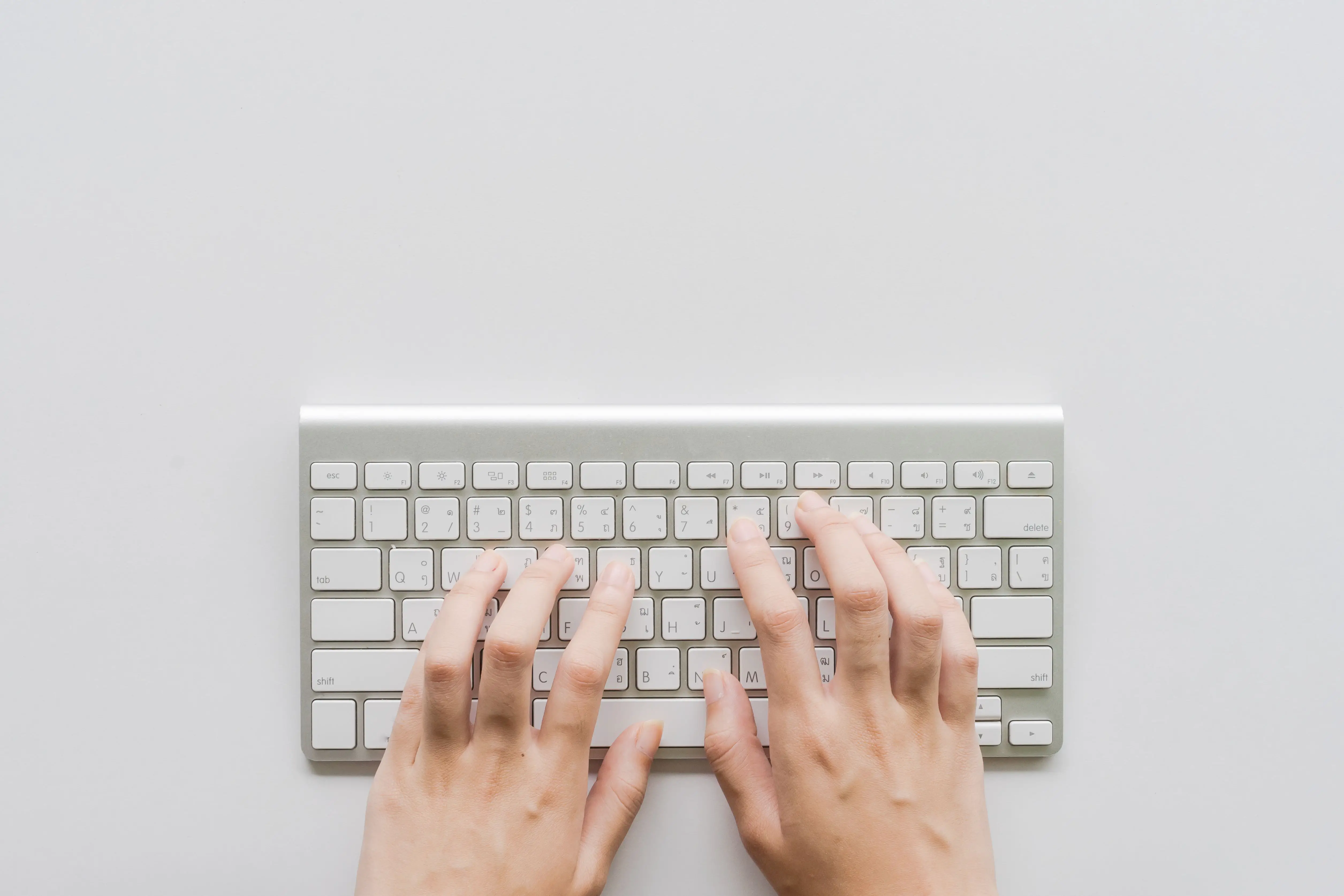 Acima, foto de uma pessoa digitando com as mãos no pequeno teclado do computador