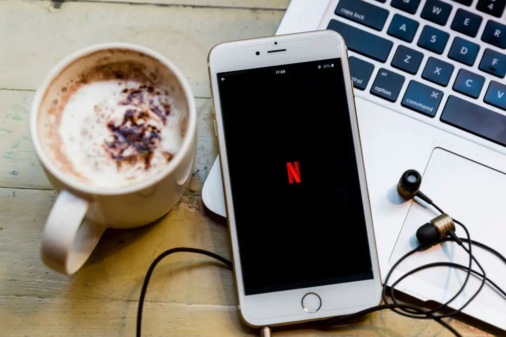 o logotipo da Netflix exibido em um smartphone que está em um laptop com uma xícara de café nas proximidades.